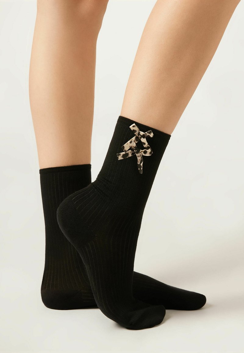 Calze nere a coste con un fiocco decorativo a stampa animale nera e beige sulla caviglia. Morbido al tatto e design a lunghezza caviglia.