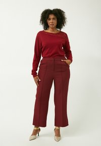 Burgunderfarbener Pullover mit Spitzenverzierungen und langen Ärmeln, kombiniert mit weit geschnittenen burgunderfarbenen Hosen, die seitliche Taschen und ein hoch tailliertes Design aufweisen.