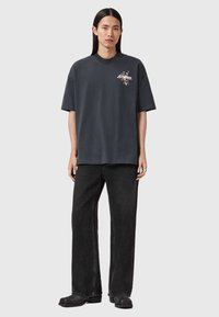 Σκούρο γκρι φαρδιά μπλούζα με στρογγυλή λαιμόκοψη, κοντά μανίκια και λουλουδένιο γραφικό σχέδιο στο στήθος, συνδυασμένη με μαύρο παντελό νι φαρδύ στο κάτω μέρος.