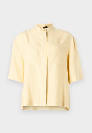 Kurzärmlige gelbe Bluse mit einem Stehkragen, ausgestattet mit zwei Fronttaschen und einer glatten Textur. Sauberes, minimalistisches Design.