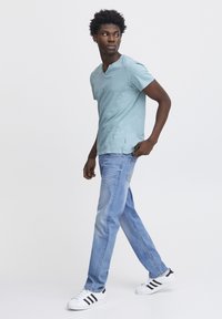 Světle modré tričko s krátkým rukávem, slim fit, v kombinaci se světle modrými džínami rovného střihu a černo-pruhovanými bílými teniskami. Jednoduchý, ležérní design.