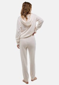 Ensemble de loungewear couleur crème comprenant un sweat à capuche et un pantalon fuselé. Texture douce, poignets côtelés et détail de taille ajustée.