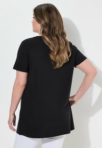 Camiseta negra de manga corta con un ajuste relajado, que presenta un dobladillo trasero ligeramente más largo. Textura suave y diseño minimalista, sin patrones adicionales.