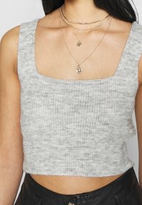 Jasnoszary krótki sweter z kwadratowym dekoltem i prążkowaną fakturą, zestawiony z warstwowanymi złotymi naszyjnikami z okrągłymi zawieszkami.