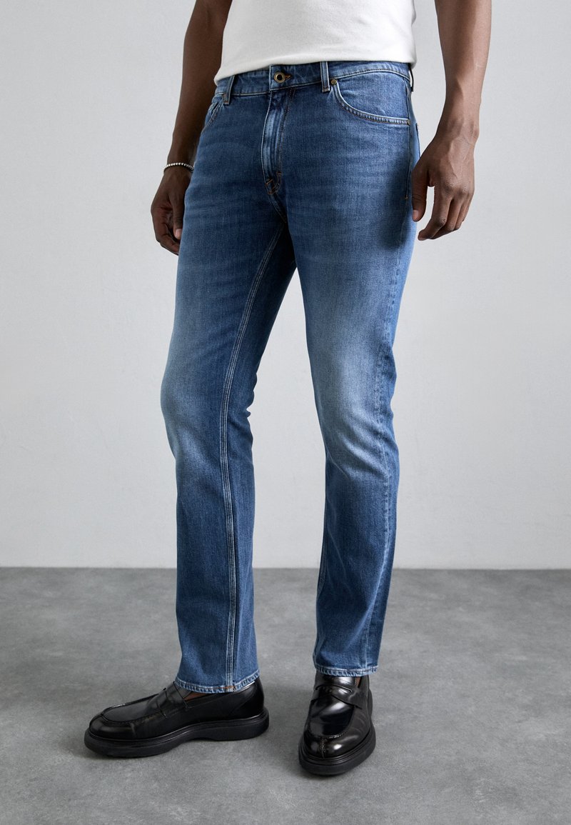 Heled sinised denim püksid sirge säärega, viie taskuga ja kerge kulumisega. Kanda mustade mokassiinide ja sobiva valge särgiga.