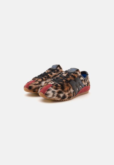 Paire de baskets basses avec fourrure imprimé léopard, détails noirs, accents en daim rouge et semelles en caoutchouc marron clair sur fond blanc.