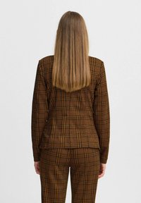 Brown checked blazer and trousers with a fitted design. Features a textured fabric with a grid pattern in black and orange accents.