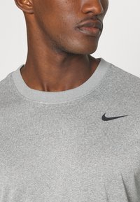 T-shirt en coton gris avec un col ras du cou et des manches courtes. Présente un petit logo Nike noir sur le haut à gauche de la poitrine. Texture lisse.