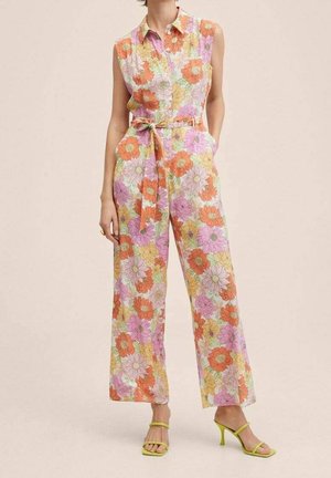 Combinaison florale avec col, sans manches, fleurs vibrantes orange, rose et jaune, taille ceinturée et pantalon large. Talons néon verts.