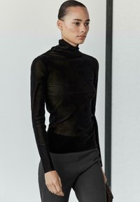 Czarny golf z miękkiego, przejrzystego materiału z długimi rękawami. Noszony z dopasowanymi ciemnymi spodniami, podkreślającymi gładką sylwetkę.