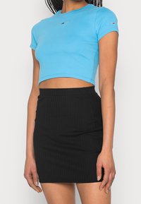 Sininen lyhythihainen croppitoppi, jossa on pieni logo, yhdistettynä mustaan ribattuun minihameeseen, jossa on elastinen vyötärö.