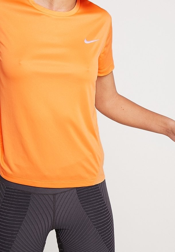 Oranžové sportovní tričko s krátkým rukávem z prodyšného materiálu, s kulatým výstřihem a malým bílým logem na levé straně hrudi.