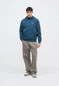 Μπλε φούτερ με κουκούλα και τσέπη καγκουρό, με λευκό λογότυπο. Συνδυάζεται με γκρι φαρδιά φόρμα και γκρι/μαύρα αθλητικά παπούτσια.