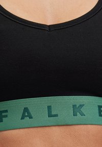 Schwarzer Sport-BH mit rundem Ausschnitt und einem breiten grünen Saum, der entlang des unteren Randes das Wort "FALK" in strukturierter Schrift zeigt.