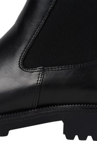 Botte en cuir noir avec des panneaux élastiques sur les côtés, surface texturée et semelle en caoutchouc robuste dotée de crampons définis pour une bonne traction.