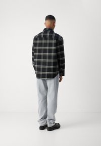 Schwarz-weißer Karohemd mit langen Ärmeln, Kragen und abgerundetem Saum; kombiniert mit hellblauen Jeans und schwarzen Schuhen.