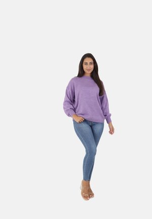 Pull en lilas tricoté avec des manches longues, des poignets côtelés et un col haut, associé à un jean skinny bleu clair et des talons transparents.