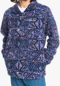 Pullover in pile con mezza cerniera, caratterizzato da motivi geometrici in tonalità blu, viola e rosa, con un logo sul petto. Tessuto morbido e strutturato.