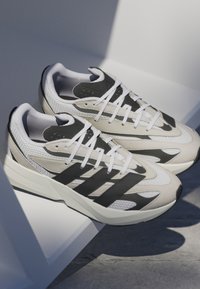 Beige and black athletic shoes feature a mesh upper, textured suede accents, padded tongue, and "LIGHTSTRIKE" branding on the sole.