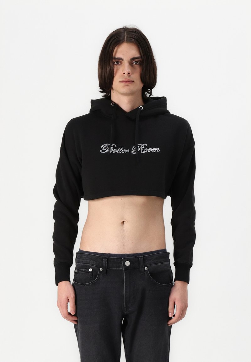 Black cropped hoodie with drawstring hood, featuring glossy "Rider Room" text in a decorative font on the front. Worn with dark jeans.