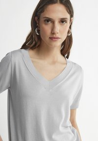 Hellgraues kurzärmeliges V-Neck T-Shirt aus weichem Stoff, mit einem klaren Schnitt und feinen Nähdetails entlang des Ausschnitts.