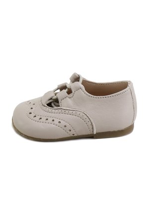 Pequeño zapato de bebé de cuero beige con patrones decorativos perforados y suela blanda, mostrado desde el lado interior.