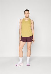Top deportivo amarillo con escote redondo, combinado con pantalones cortos burdeos. Calcetas blancas y zapatillas deportivas con detalles en rosa completan el atuendo.