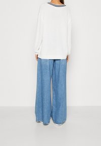 Vit stickad tröja med långa ärmar och en marinrandig halsringning, ihop med lösa, ljusblå vida jeansbyxor.