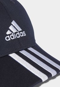 Casquette bleu marine en tissu avec trois rayures blanches et un logo "adidas" brodé en blanc sur le devant.