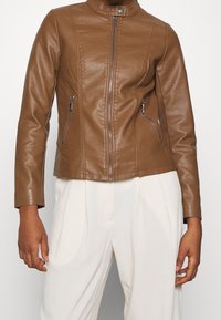 Veste en cuir marron au design ajusté, col montant et fermeture éclair à l'avant. Comprend deux poches latérales zippées et une texture lisse.