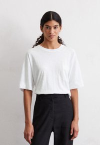 T-shirt blanche à manches courtes en coton léger, avec une poche poitrine. Associée à un pantalon noir ajusté pour un look décontracté.