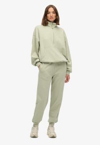 Lys grøn sweatshirt med høj hals, frontlomme og løs pasform, parret med matchende sweatpants. Har ribbede manchetter og ankler.