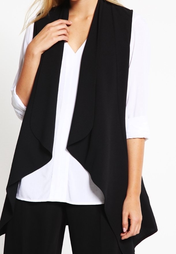 Personne portant une chemise blanche à boutons avec manches retroussées et un gilet noir fluide sans manches et ouvert devant.