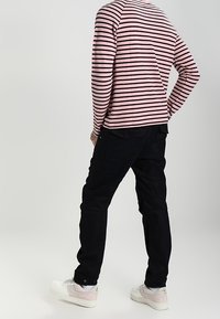 Camisa de rayas de manga larga en rosa y negro, combinada con pantalones negros y zapatillas blancas. La camisa presenta un diseño de raglán.