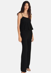 Čierny, textúrovaný dvojdielny outfit s peplum topom na tenkých ramienkach a priliehavými dlhými nohavicami. Minimalistický dizajn s uvoľnenou siluetou.