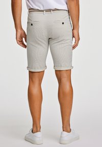 Pantalones cortos de tela gris claro con un patrón texturizado, con puños enrollados, dos bolsillos traseros con botones, combinados con zapatillas blancas.