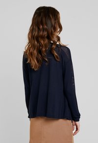 Granatowy sweter z długim rękawem o luźnym kroju, z siateczkowymi panelami bocznymi i ściągaczami, wykonany z miękkiego materiału.