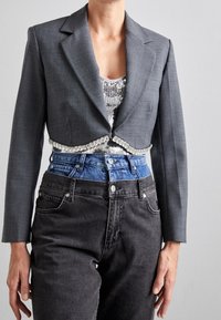 Blazer gris recortado con un brillante adorno de cuentas, combinado con una blusa de lentejuelas y jeans negros de talle alto.
