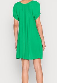 Grøn kortærmet kjole lavet af letvægtsstof, med plisseret rygdesign og knapdetaljer på ærmerne.