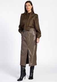 Bruine metallic blouse met lange mouwen, een striknek en gepofte schouders, gecombineerd met een midi-rok van bruine faux-leer met een split aan de voorkant en zakken.