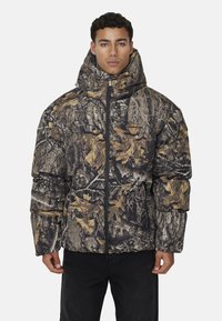 Kurtka puchowa w kamuflażu, w mieszance ciemnej zieleni, brązu i beżu, z wysokim kołnierzem, zapięciem na zamek i teksturowanym materiałem.