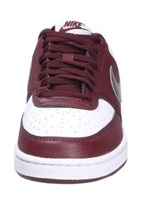 Baskets Nike en bordeaux et blanc, avec une tige en cuir, une boîte à orteils perforée, des lacets ronds et un logo Nike argenté sur le côté.