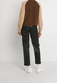 Braun-beige farbblockierter Pullover mit gerippter Textur, kombiniert mit schwarzen Lederhosen und weißen Sportschuhen.