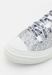 Baskets pailletées argentées avec une semelle blanche épaisse et des lacets blancs imprimés du texte « LOVE MOSCHINO » en noir.