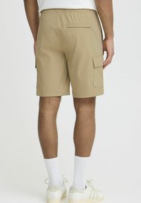 Beige cargo shorts made of lightweight fabric, featuring side pockets, a single back pocket, and an elastic waistband, above white socks and shoes.