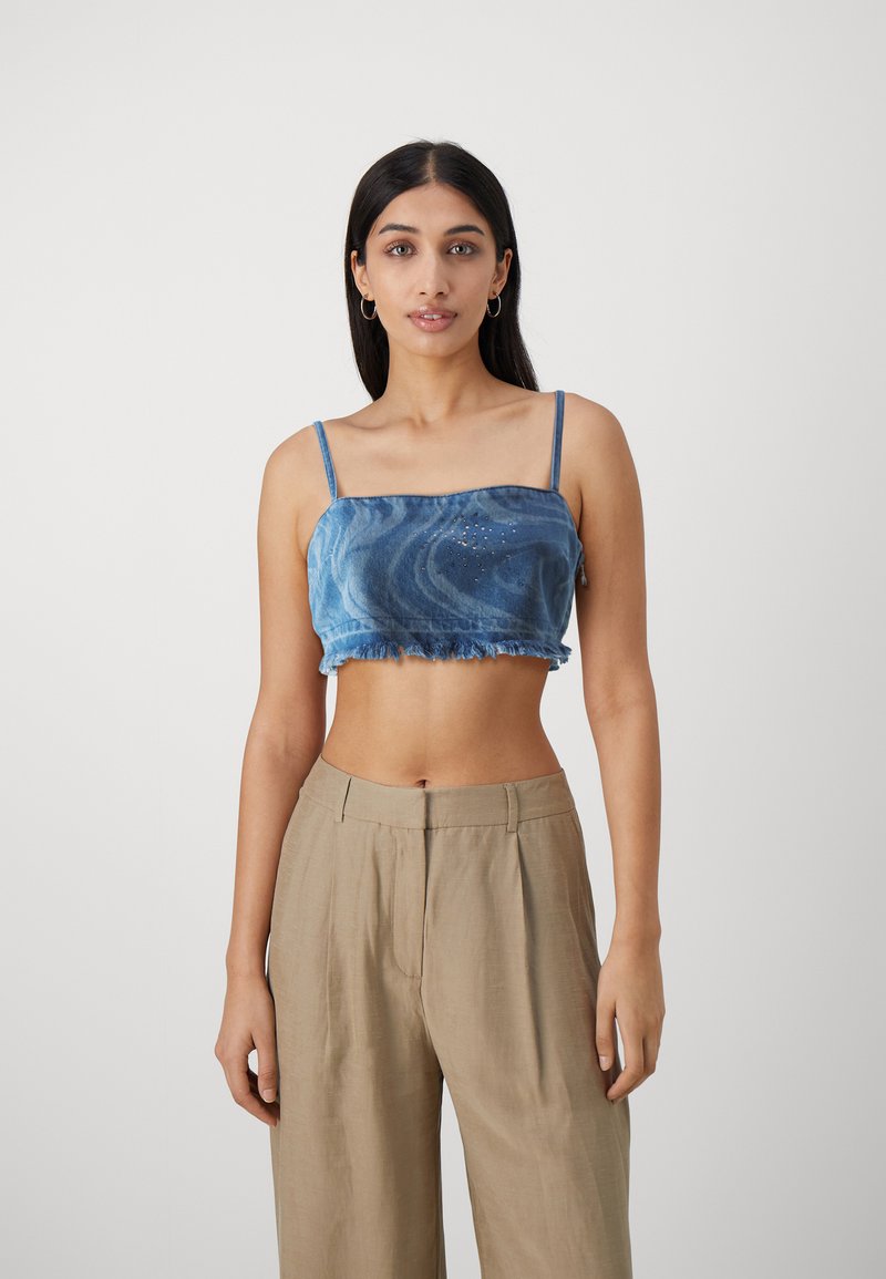 Avskåret blå denimtop med spaghettistropper, frynsete kant og subtile pyntedetaljer. Kombinert med lys beige, løstsittende bukser.
