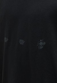 Μαύρο ύφασμα με αχνό γκρι κείμενο και λογότυπα, συμπεριλαμβανομένων των "Athletic Club" και μικρό λογότυπο Nike στο δεξί μέρος.