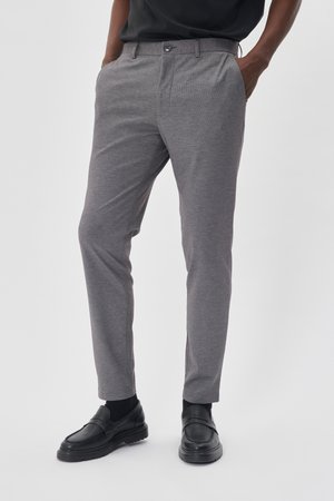 Graue maßgeschneiderte Hose mit einem subtilen Karomuster, ausgestattet mit Fronttaschen und einem Knopfverschluss, kombiniert mit schwarzen Slippern.