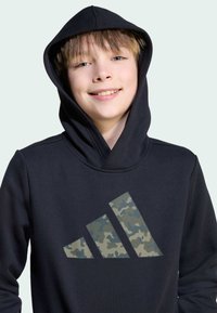 Black hoodie made of soft fabric with a large camo-patterned Adidas logo on the front. Features a drawstring hood and ribbed neckline.