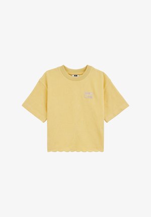 Geltonas trumpomis rankovėmis trumpintas megztinis su banguotu apačios kraštu ir mažu pleistru ant krūtinės su tekstu ir grafinio dizaino elementu.